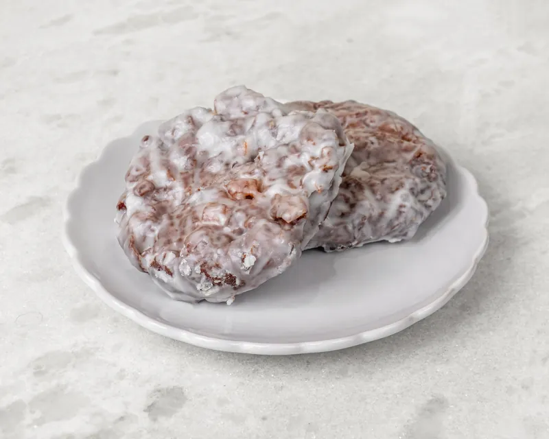 Two glazed apple fritters on a white plate